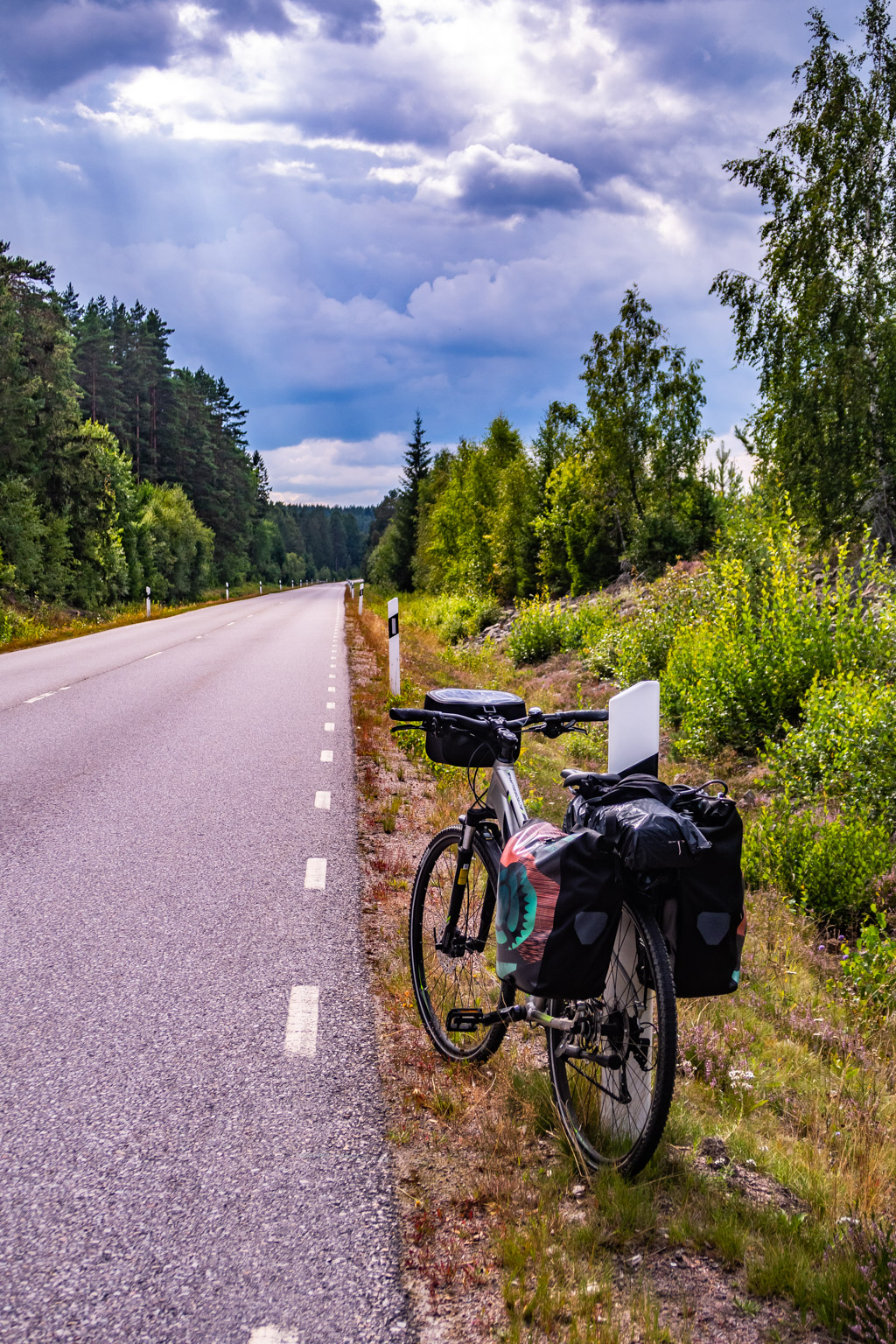 Cykel med packväskor parkerad vid sidan av en asfaltväg en molnig men vacker sommardag i Småland. 