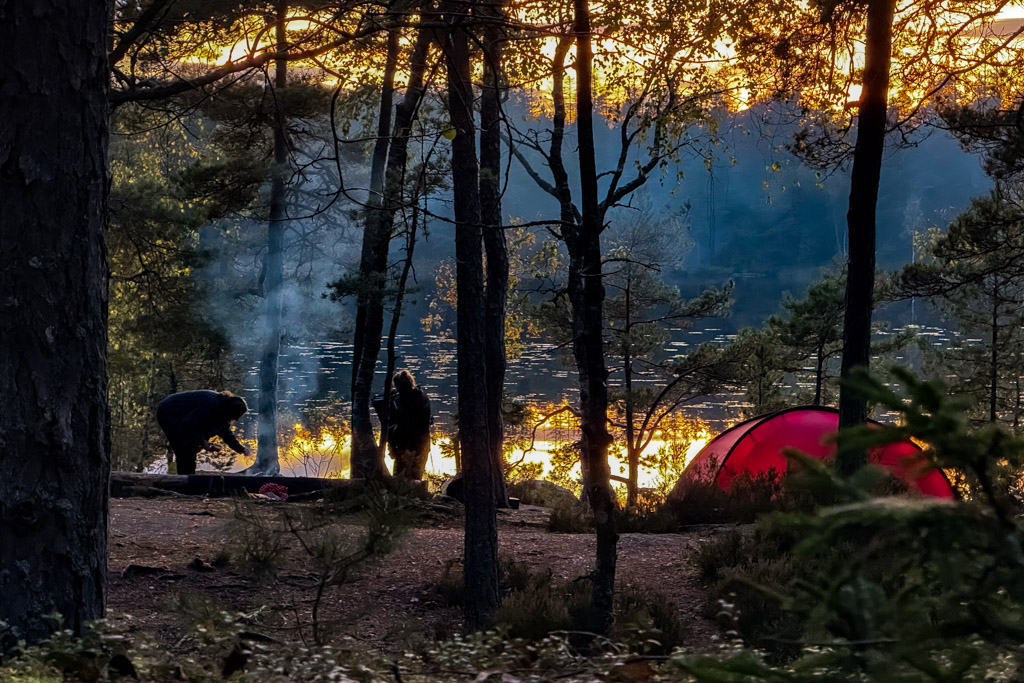 Lägerplats med människor och tält i solnedgången, sett från avstånd.